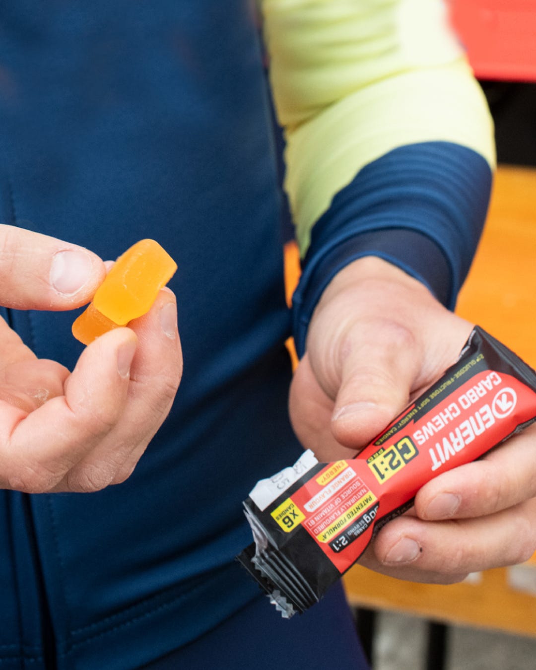Cyclist holding an Enervit Carbo Chews C2:1PRO Orange pack and an orange chew